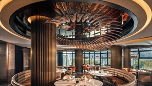 Un restaurante moderno con una zona de estar circular central, amplios ventanales con vistas a la ciudad y un diseño de techo singular.
