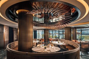 Restaurante moderno com área de estar circular central, janelas amplas com vista para a cidade e design de teto único.