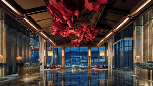Un vestíbulo amplio con suelo reflectante, grandes ventanales con vistas a la ciudad y un diseño único de techo floral en rojo.