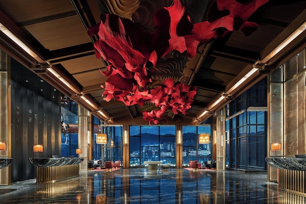 Un vestíbulo amplio con suelo reflectante, grandes ventanales con vistas a la ciudad y un diseño único de techo floral en rojo.