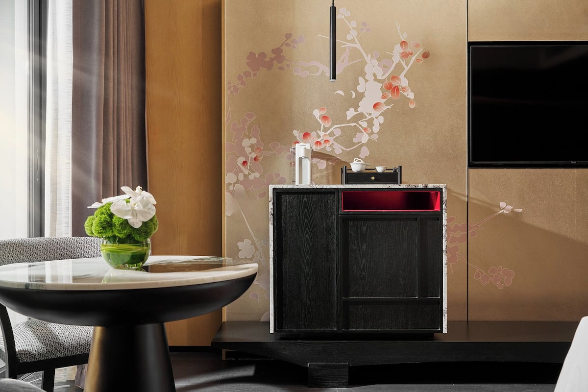 A modern hotel room with a round table, a decorative vase with flowers, a black and red cabinet, and a wall-mounted TV.