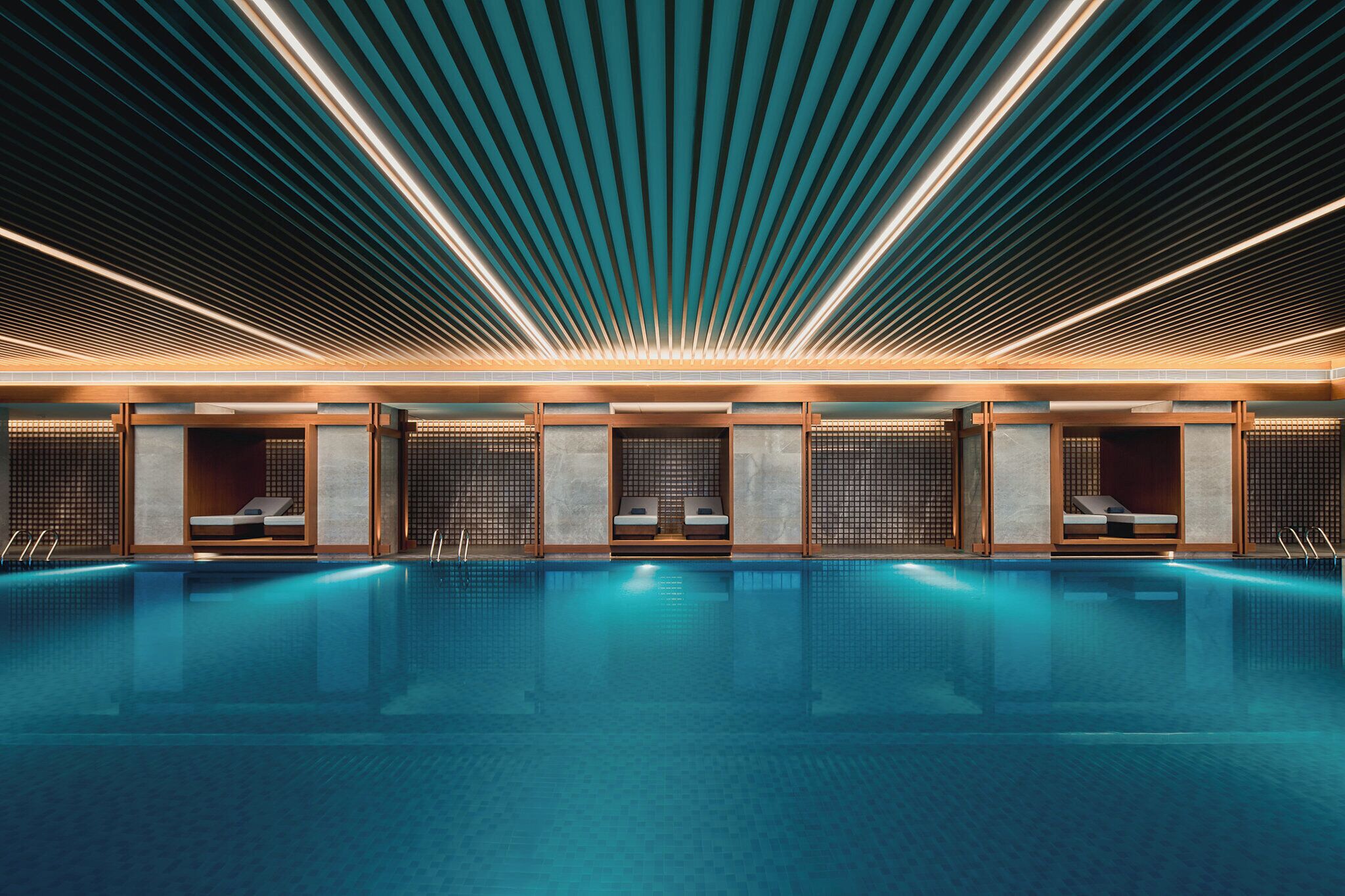A modern indoor swimming pool with a sleek design, featuring a long, narrow pool and a ceiling with linear lighting.