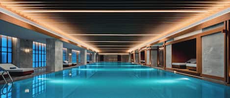 A modern indoor swimming pool with a sleek design, featuring a long, narrow layout and a central water feature.