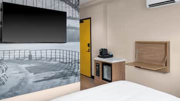 A hotel room with a large flat-screen TV, a wooden cabinet with a coffee machine, a small refrigerator, and a wooden shelf.