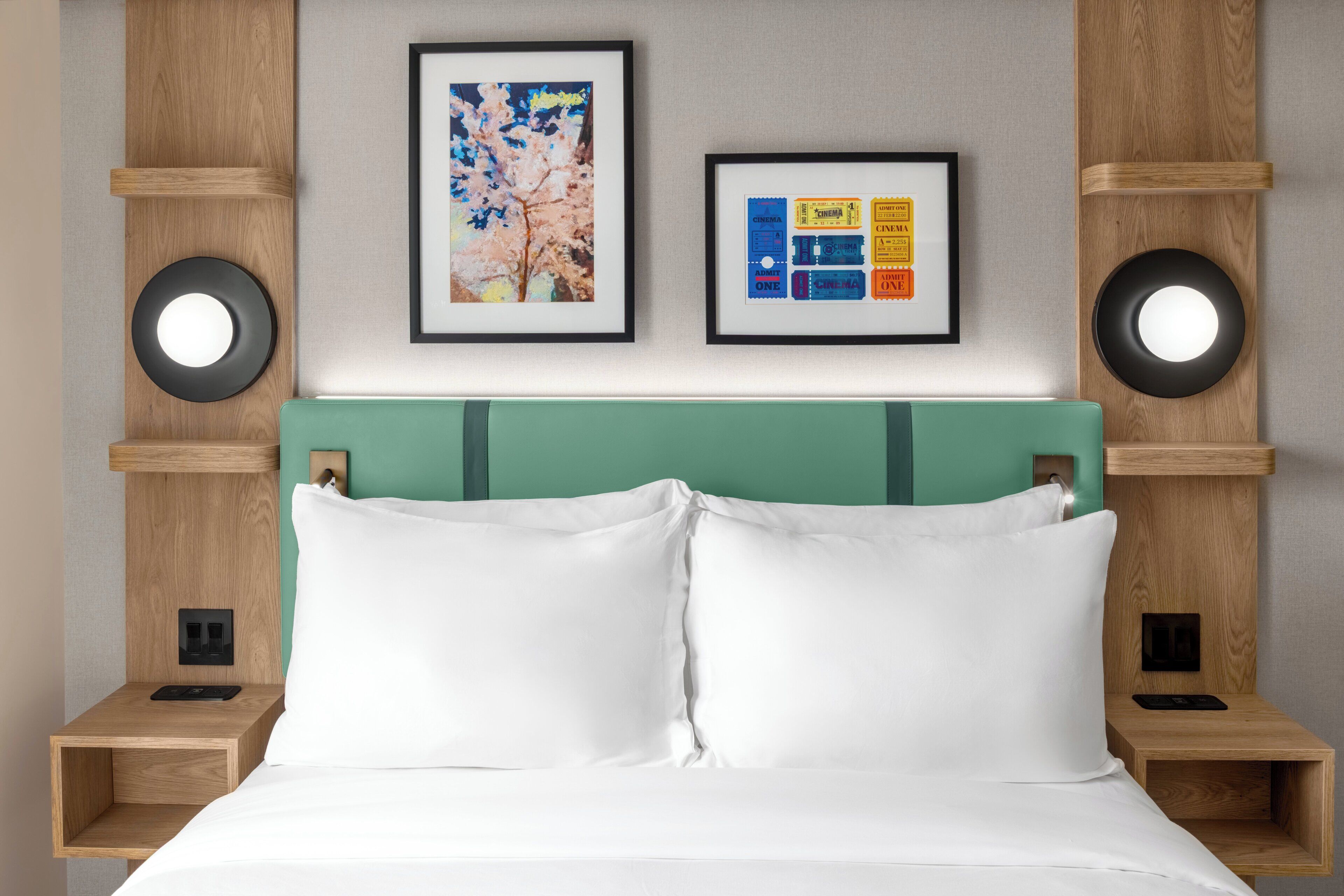 Een bed met witte lakens, een groen hoofdeinde en twee nachtkastjes met zwarte klokken.