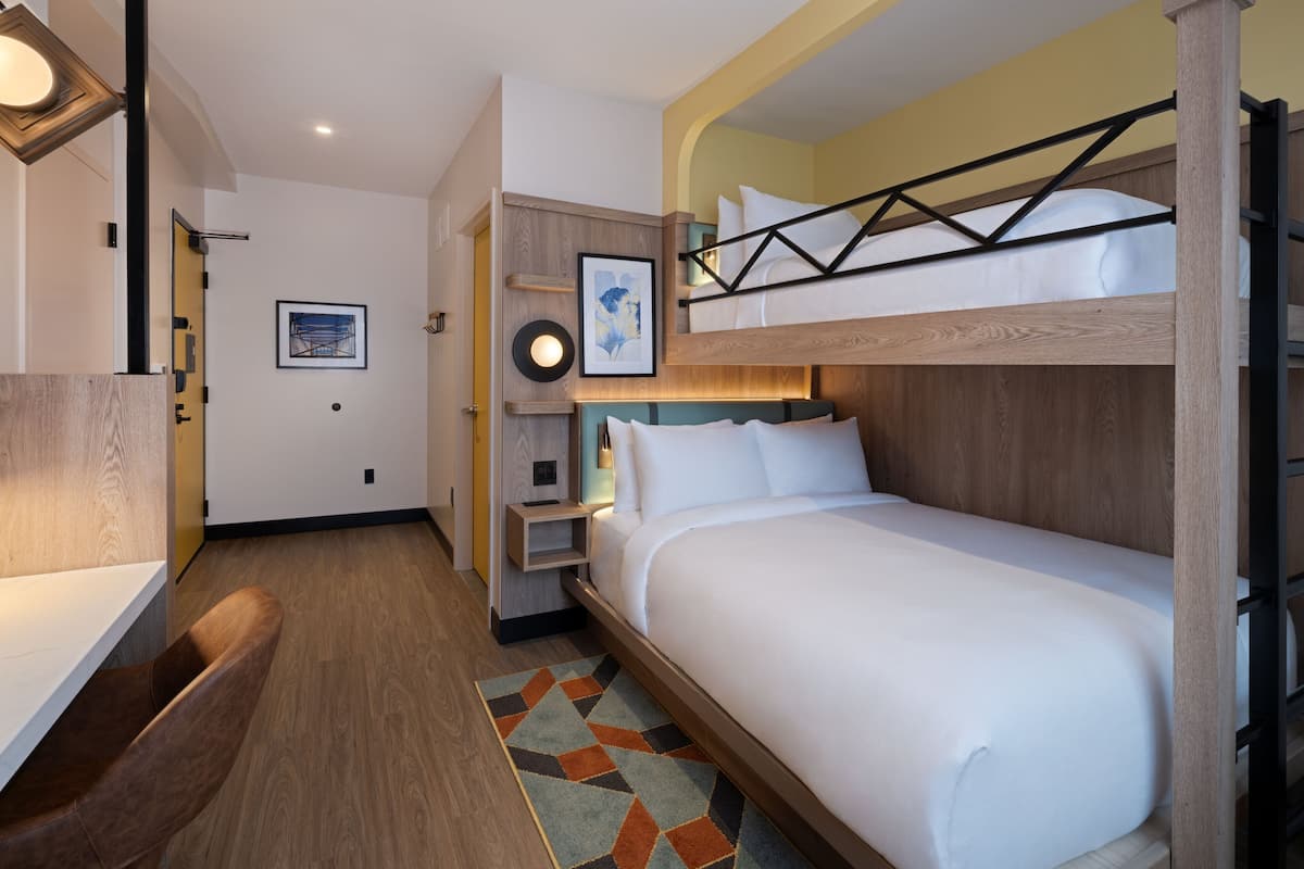 Une chambre d’hôtel avec un lit superposé, un bureau et un petit coin salon.