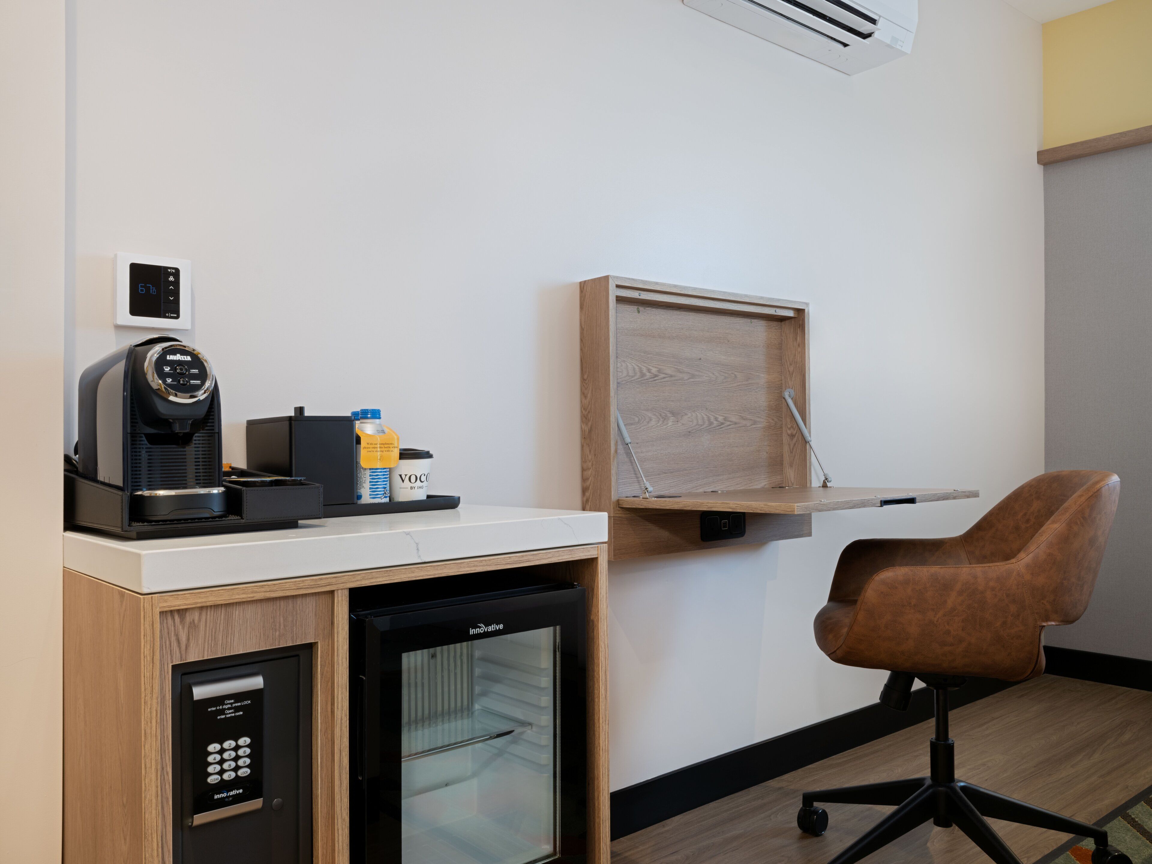 Une chambre d’hôtel compacte équipée d’une kitchenette, d’un réfrigérateur, d’une machine à café, d’une petite table, d’une chaise et d’un bureau pliant.