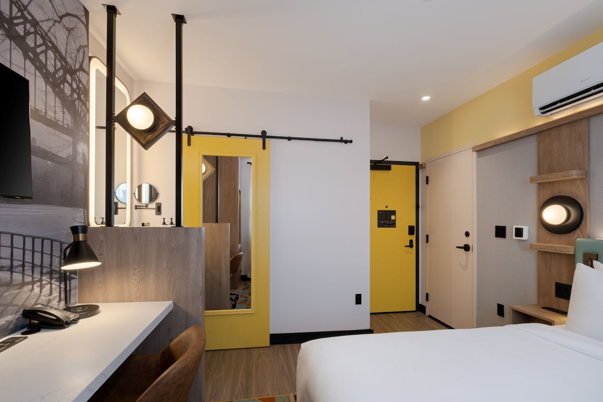 Una habitación de hotel moderna con una cama, un escritorio con lámpara, un espejo y un armario.