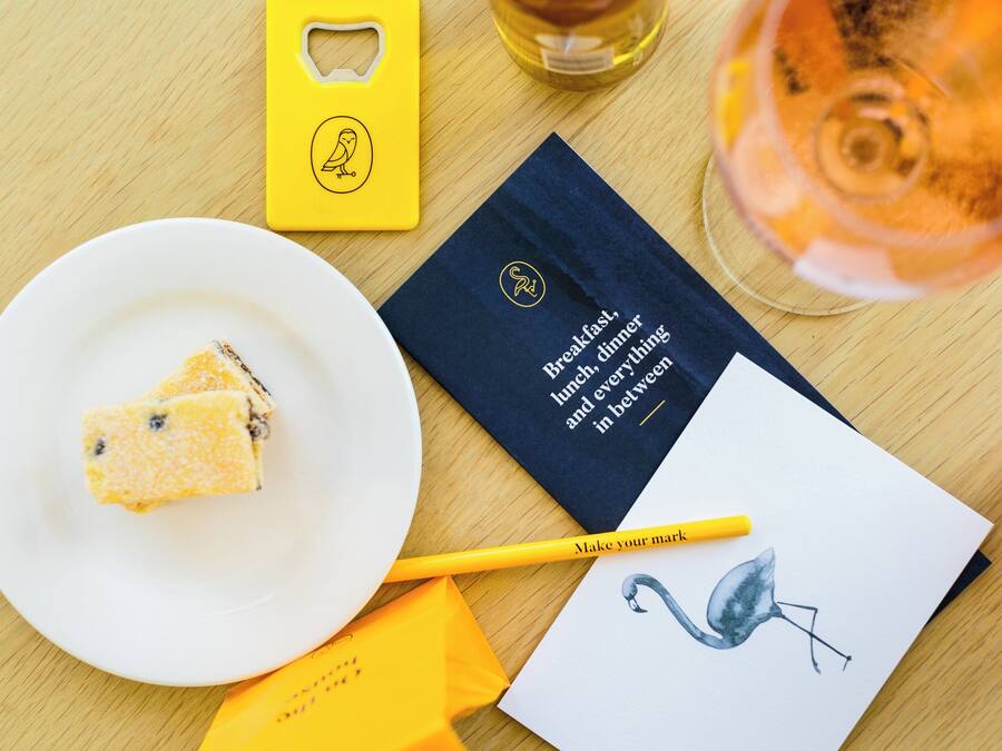 A table with a slice of cake, a wine glass, a notebook, and a yellow box.