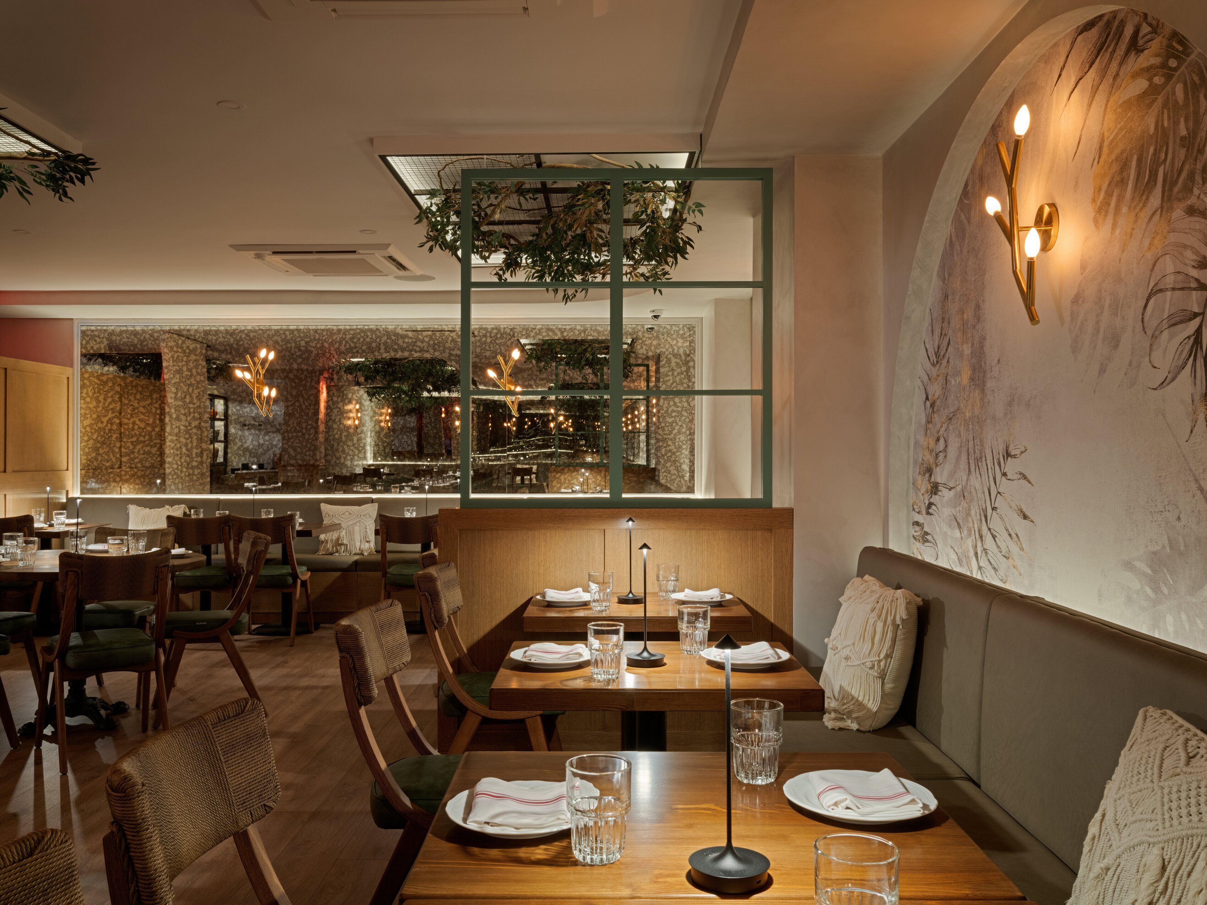 A restaurant with wooden tables and chairs, a large window with a view of the street, and a wall with a floral mural.