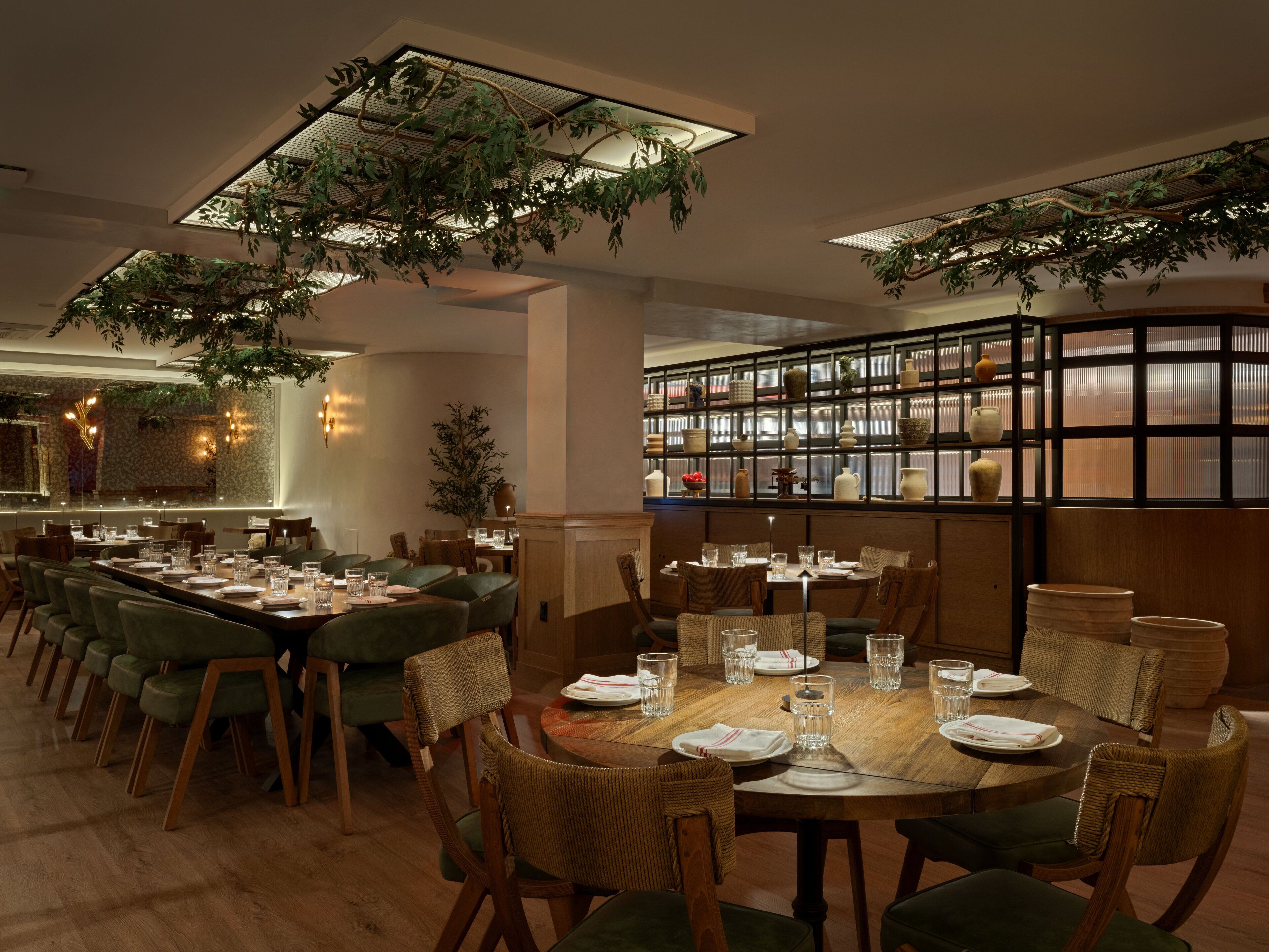 A restaurant with a long dining table, multiple chairs, and hanging plants.