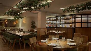 A restaurant with a long dining table, multiple chairs, and hanging plants.