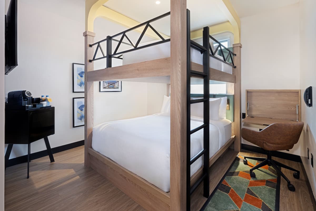 Une chambre avec un lit superposé, un bureau et une chaise, un téléviseur à écran plat et des œuvres d’art accrochées aux murs.