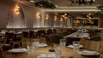 A restaurant interior with round tables, chairs, and a long bench seating area.