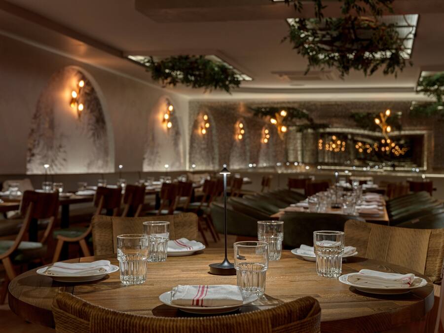 Een restaurantinterieur met ronde tafels, stoelen en een lange zithoekbank.