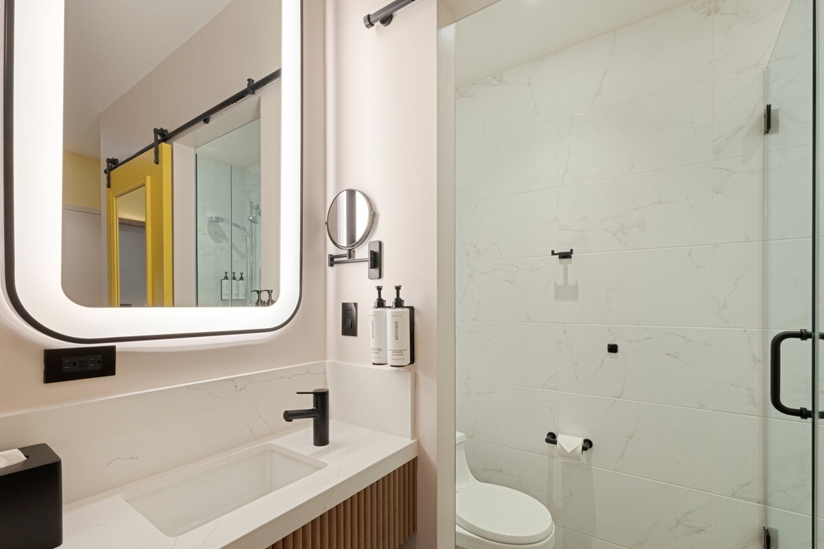 Un baño moderno con tocador blanco, un espejo grande, un inodoro y una cabina de ducha de vidrio.