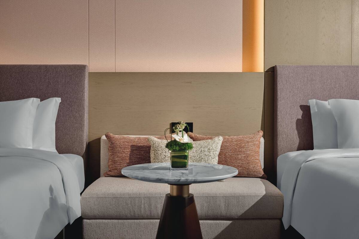 A hotel room with two beds, a round table with a vase, and a large headboard.