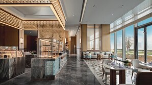 Un moderno vestíbulo de hotel con una recepción de mármol, zona de estar y amplias ventanas que ofrecen vistas al exterior.