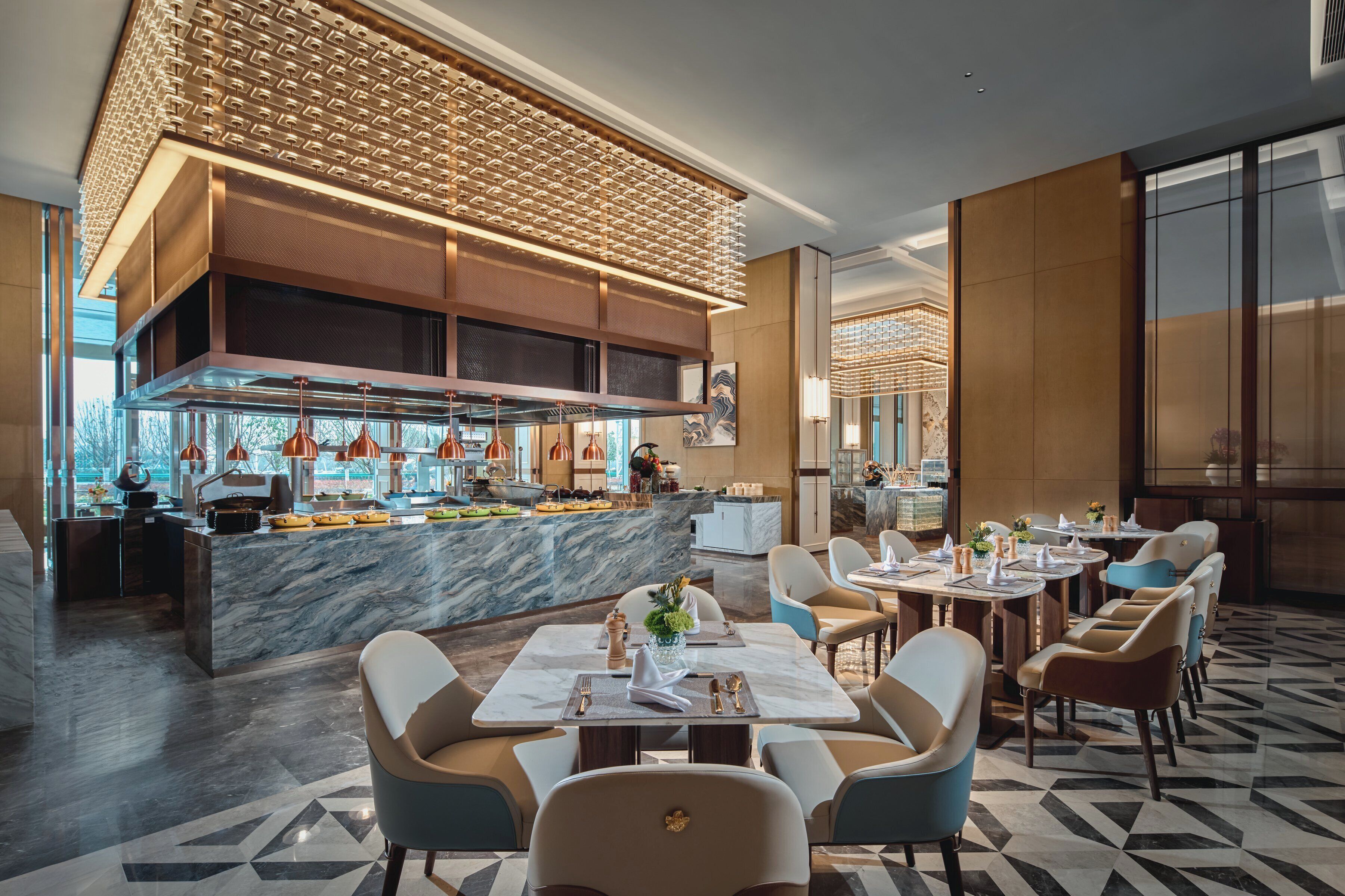 Un restaurante moderno con mostradores de mármol, una barra central y una variedad de opciones de asientos, incluyendo mesas redondas y sillas acolchadas.