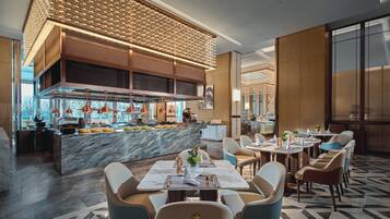 Un restaurante moderno con mostradores de mármol, una barra central y una variedad de opciones de asientos, incluyendo mesas redondas y sillas acolchadas.
