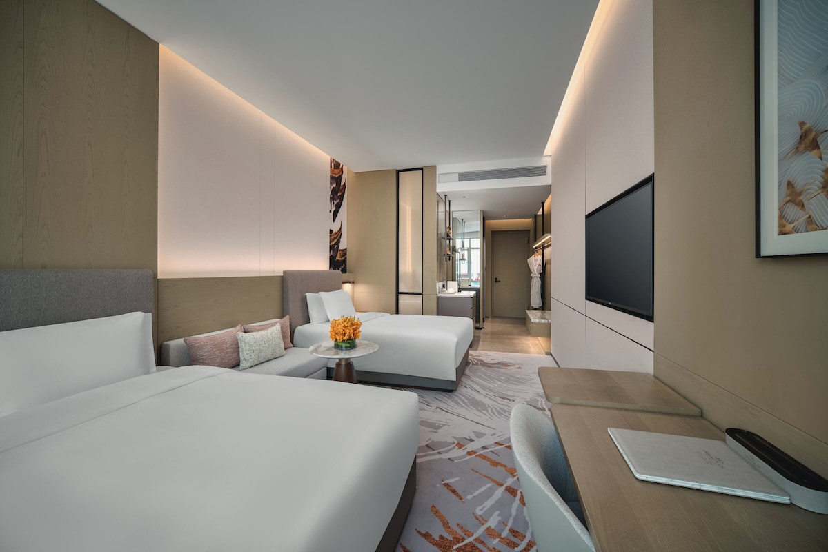 Una habitación de hotel moderna con una cama grande, un sofá, un escritorio con una computadora portátil y un televisor.