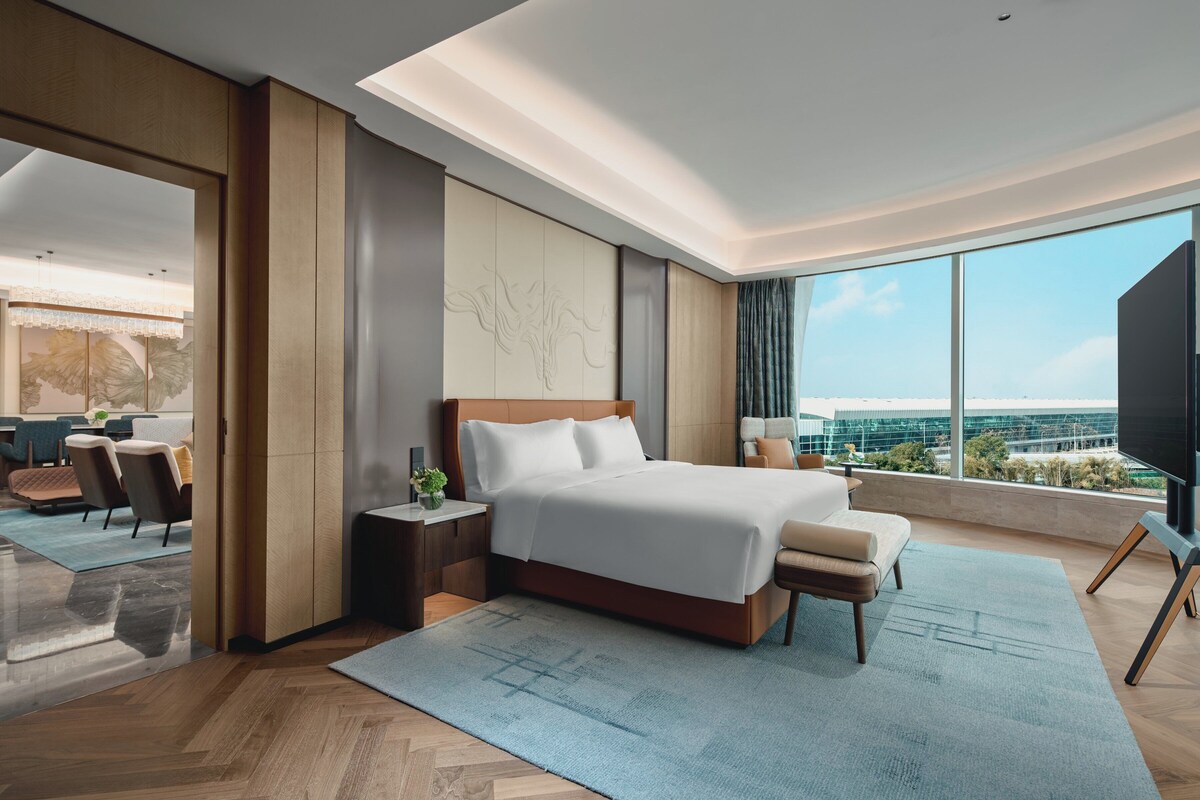 Una habitación de hotel moderna con una cama grande, vistas a la ciudad y un balcón con zona de estar.