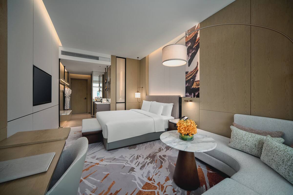 A modern hotel room with a bed, a sofa, a dining table, and a TV.