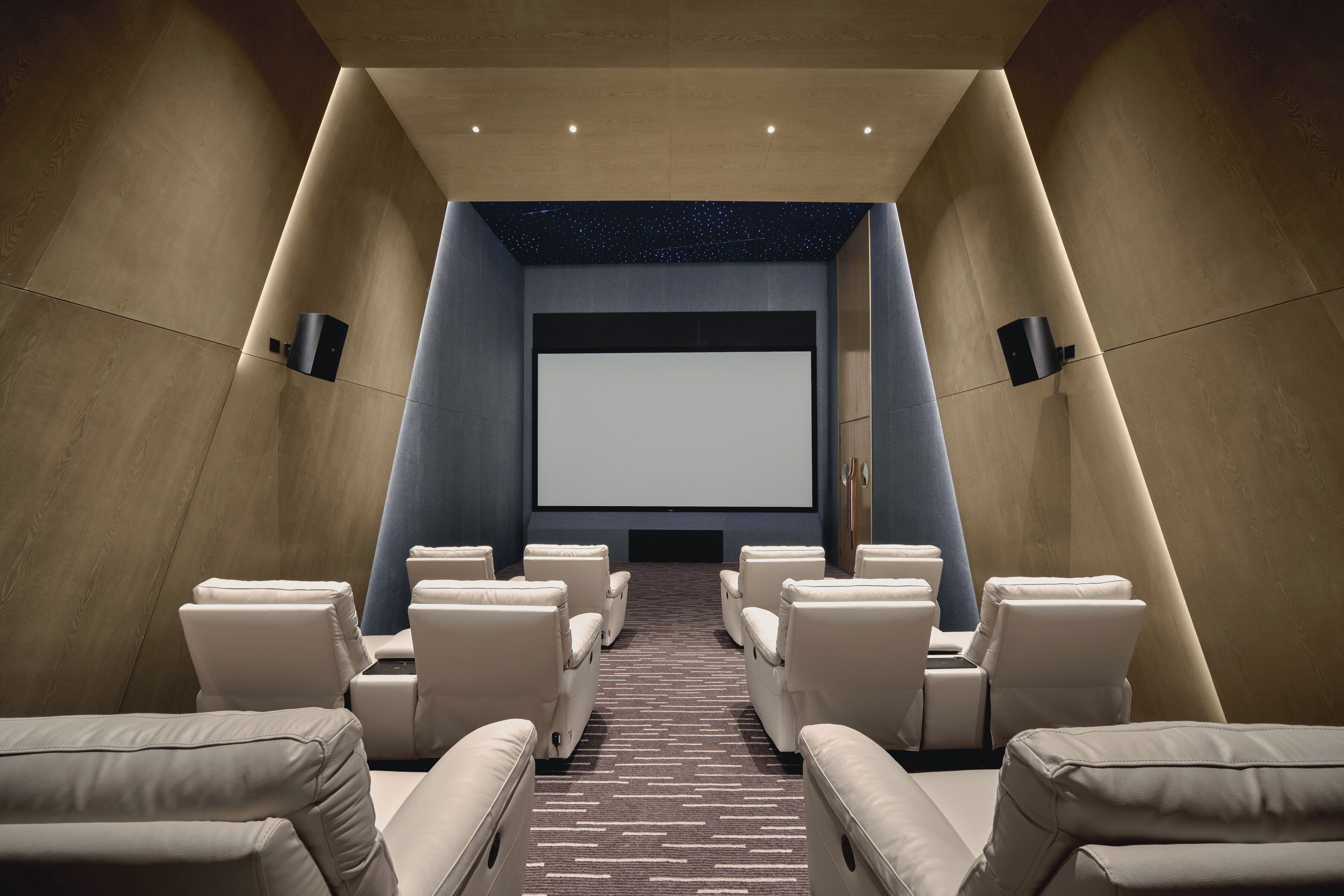 A modern home theater with plush seating arranged in a semi-circle facing a large screen.