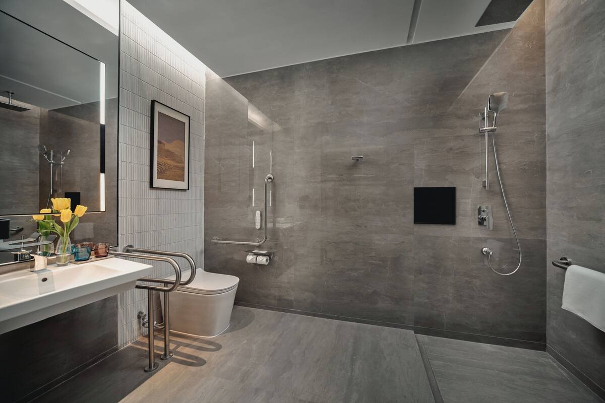 A modern bathroom with a large mirror, a toilet, a shower area, and a sink with a towel rack.