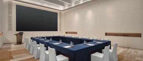 Una sala de conferencias con una larga mesa, sillas blancas y una pantalla grande.