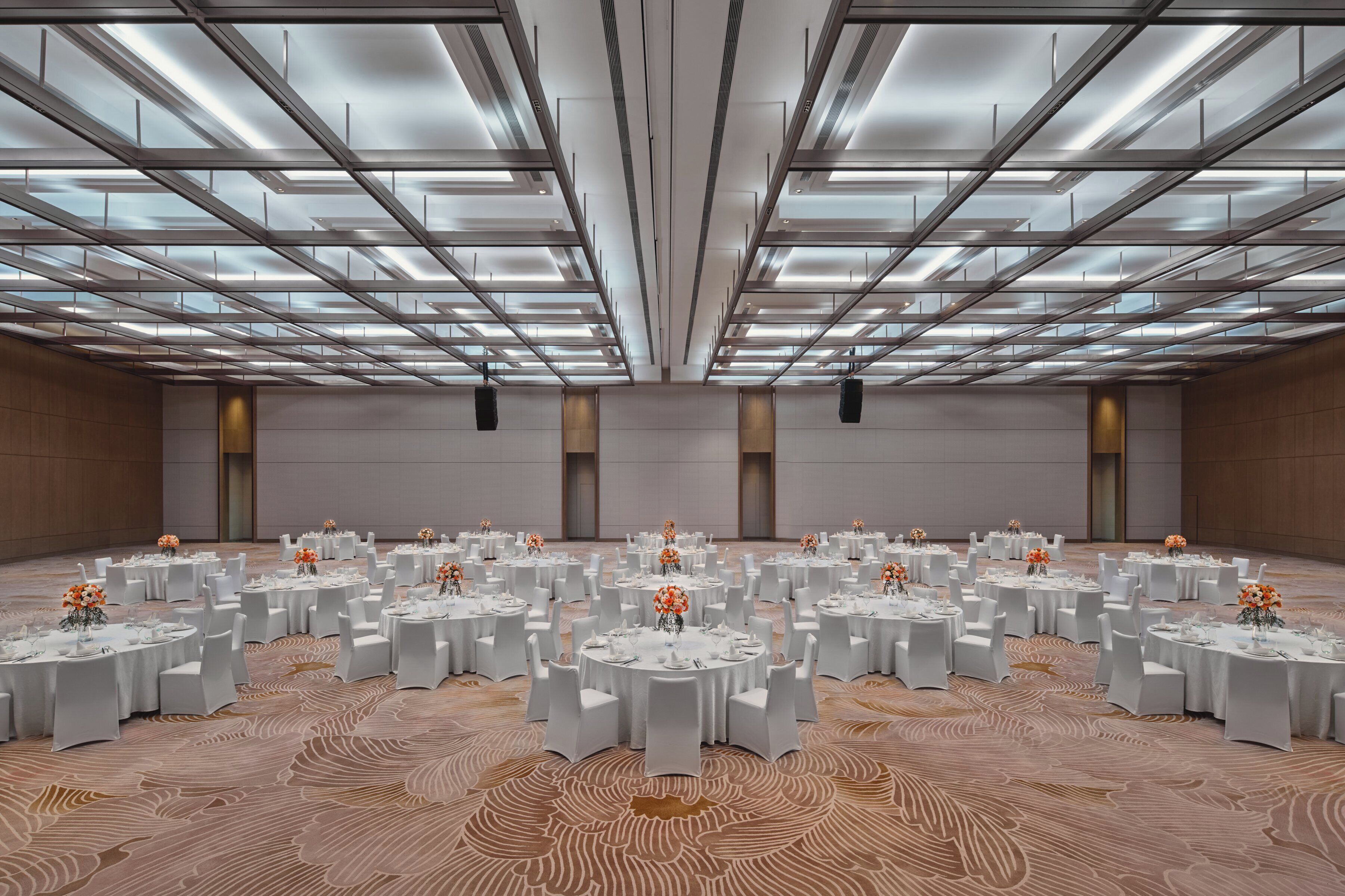 A large conference room with multiple round tables, white chairs, and floral centerpieces.