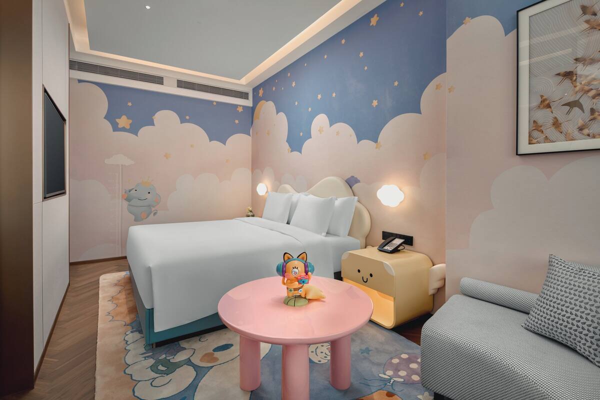 A bedroom with a bed, bedside table, nightstand, and a small round table with a toy.