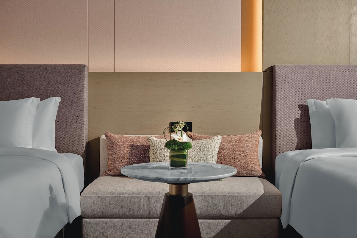 A hotel room with two beds, a round table with a vase, and a large headboard.