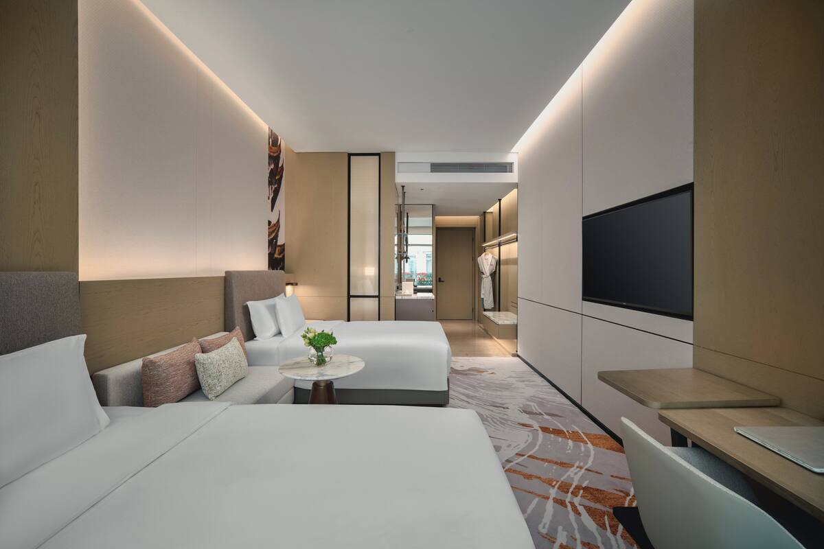 A modern hotel room with a large bed, a smaller bed, a desk, and a TV.