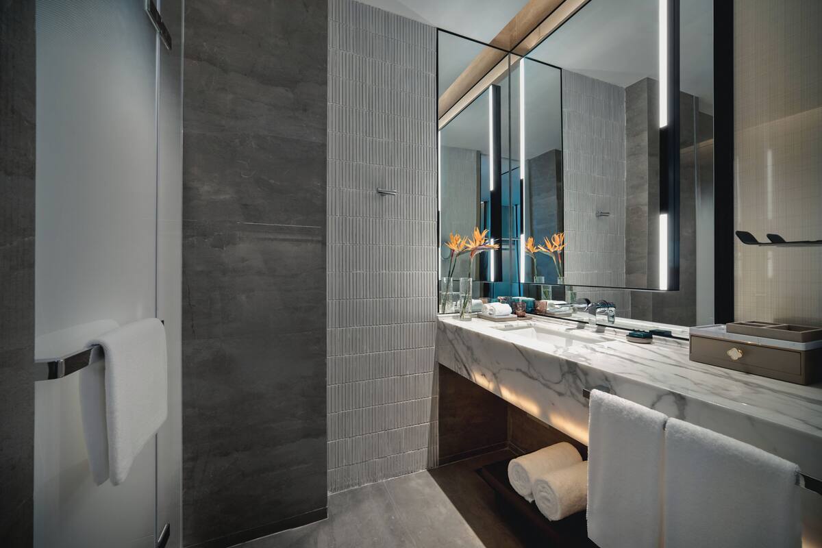 A modern bathroom with a large mirror, marble countertop, and a towel rack.