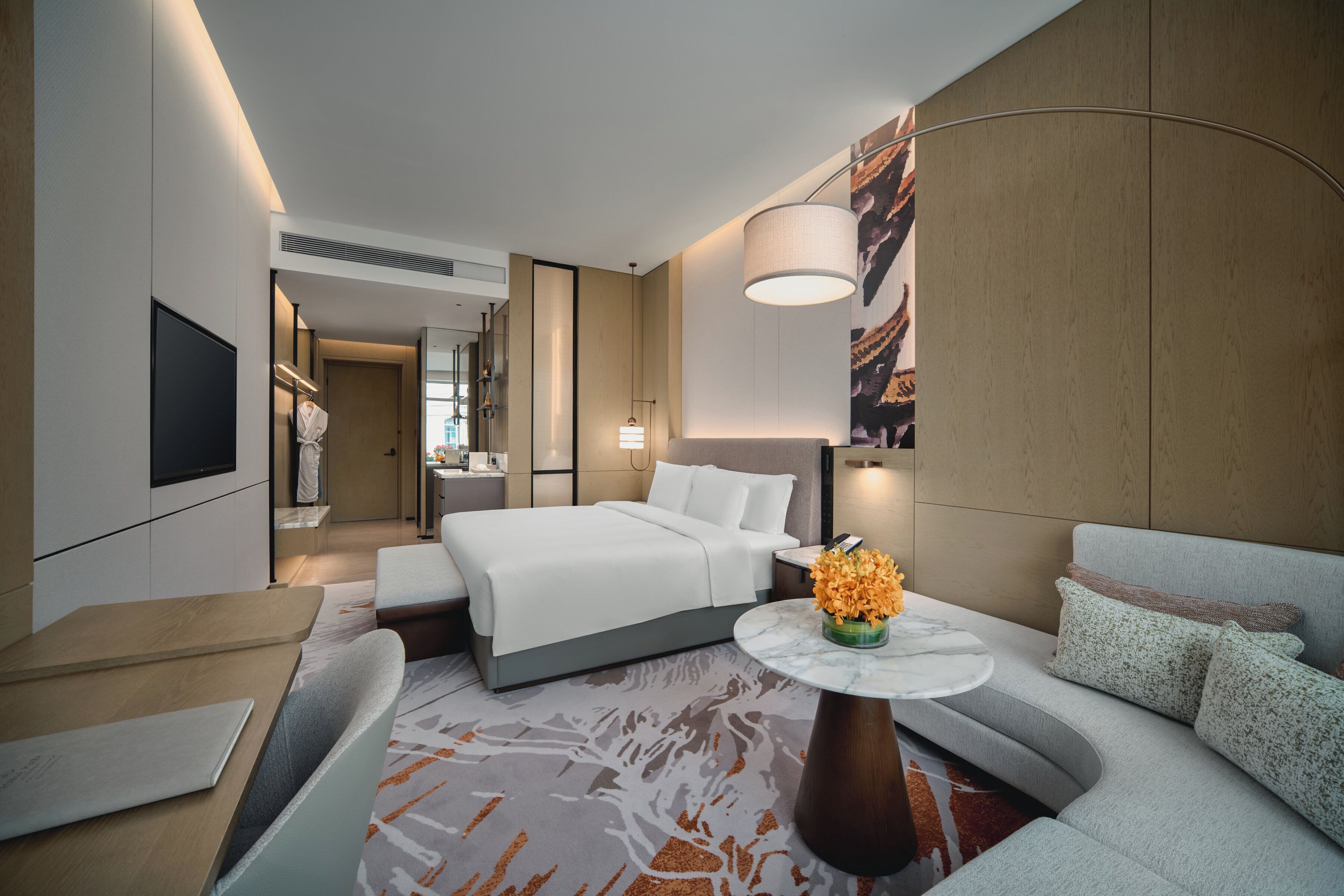 A modern hotel room with a bed, a sofa, a dining table, and a TV.
