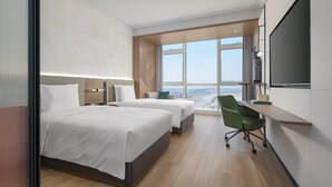 Una habitación de hotel moderna con dos camas, un escritorio, una silla y un ventanal con vistas a la ciudad.