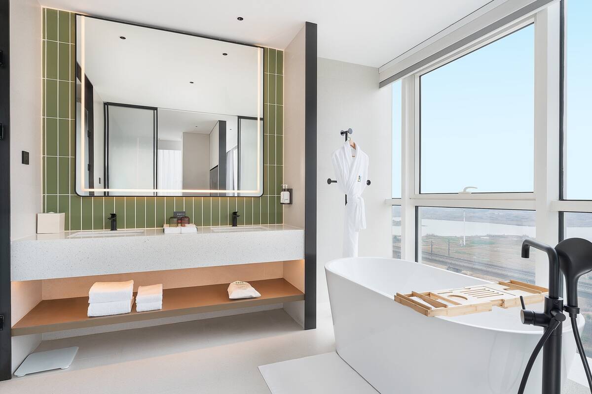 A modern bathroom with a large mirror, a bathtub, and a view of a bridge through the window.