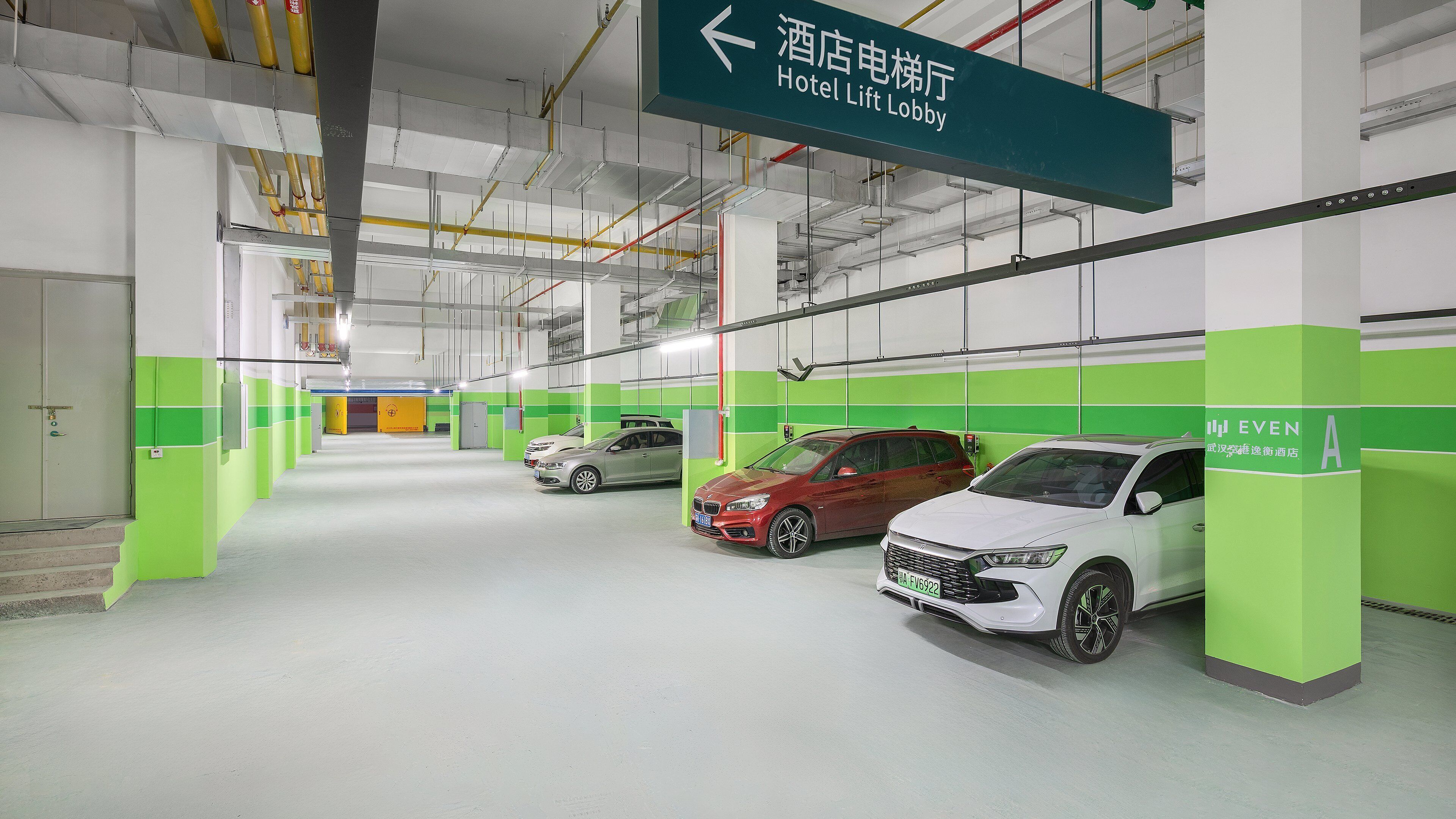 A parking garage with multiple levels, green pillars, and a sign indicating the direction to the hotel lift lobby.