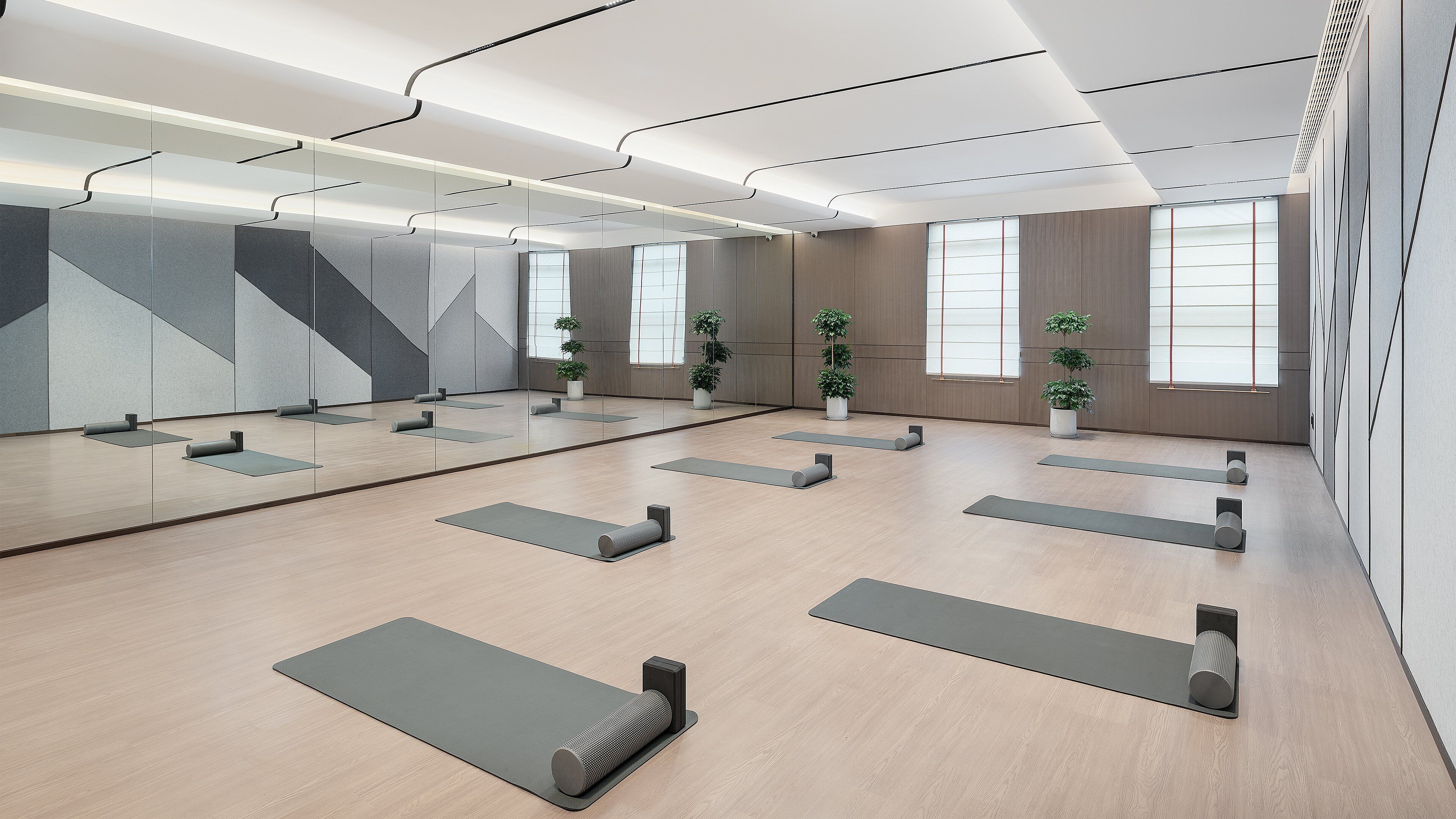 A modern yoga studio with wooden floors, mirrored walls, and large windows.