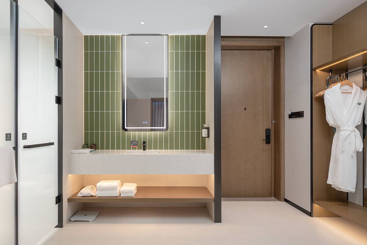 A modern bathroom with a large mirror, green-tiled wall, and a robe rack.