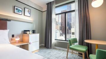Hotelkamer met een bed, een bureau met lamp, een stoel, een tafeltje en een raam met gordijnen.