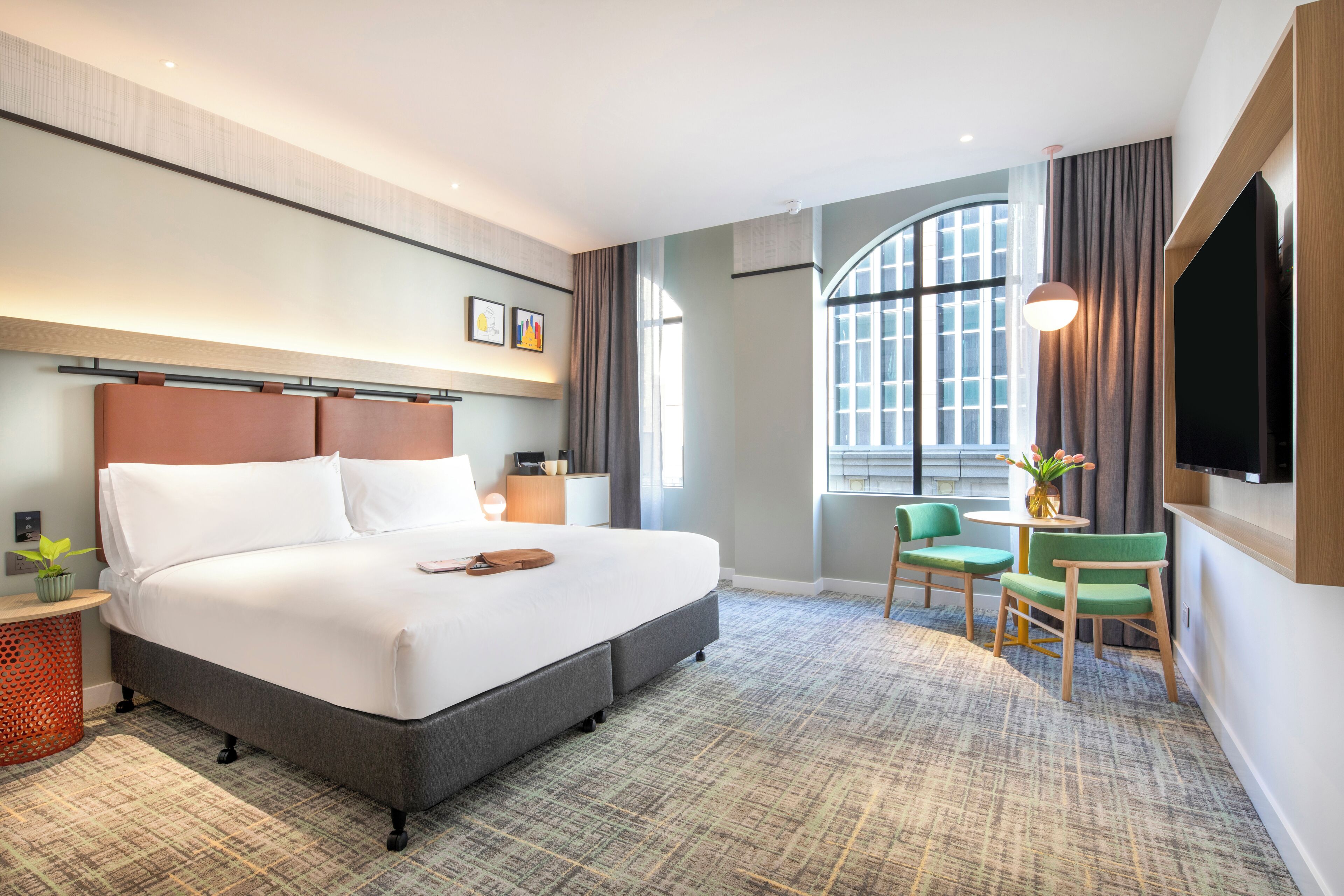 A hotel room with a large bed, a desk with a chair, a TV, and a window with curtains.
