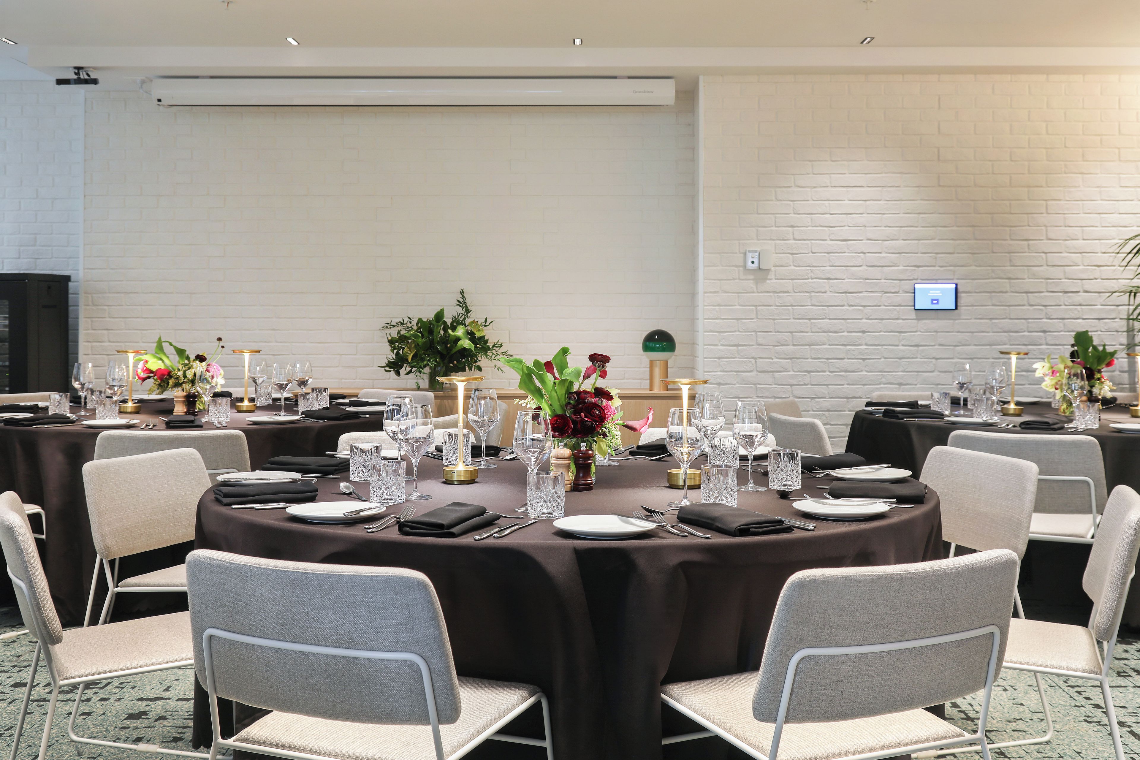 A conference room with round tables, chairs, and a white brick wall.