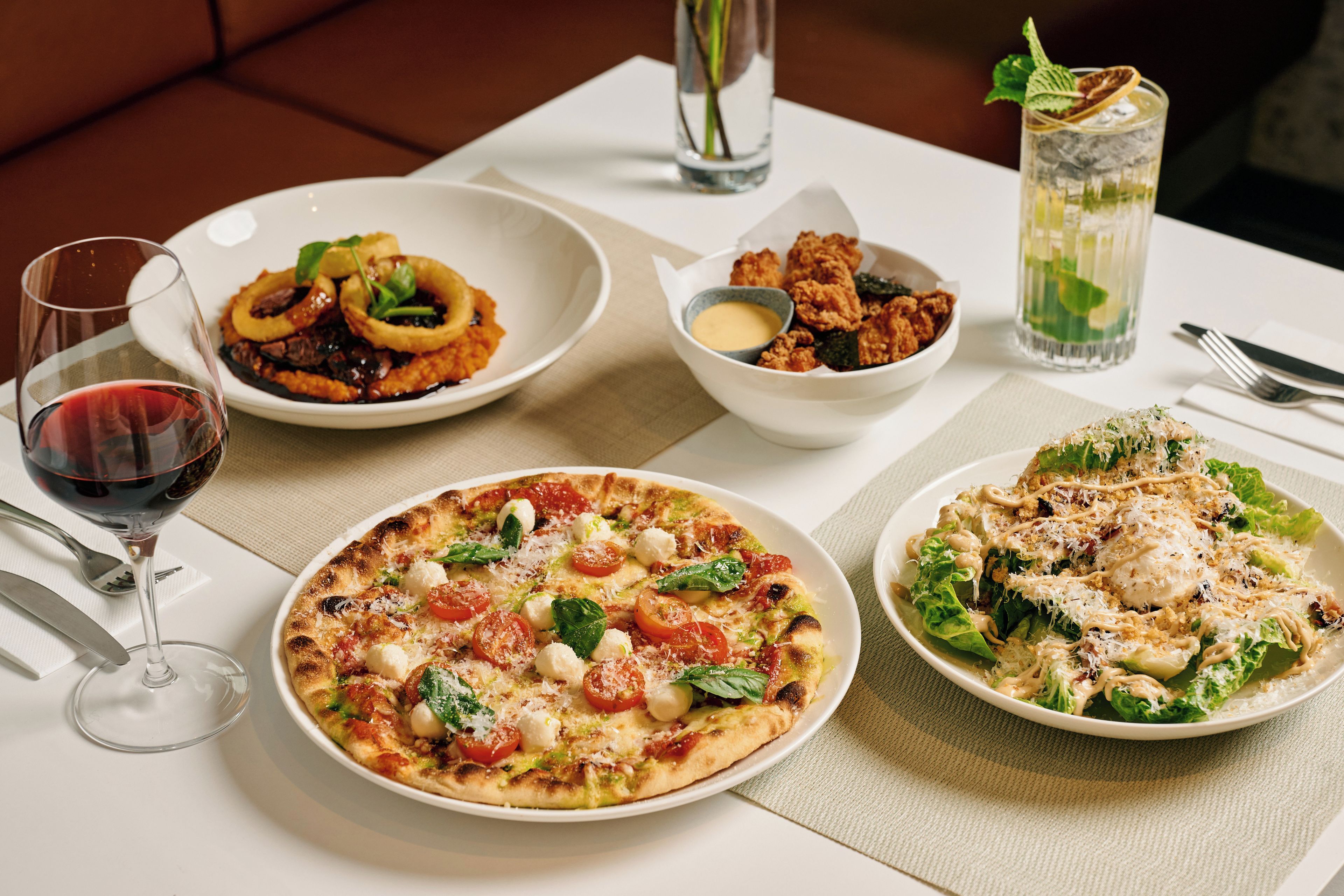 A table set with a variety of dishes including pizza, salad, and fried items, along with a glass of red wine and a glass of water.