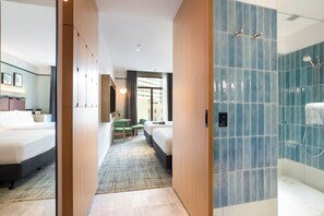 Een hotelkamer met een bed, een bureau, een stoel en een badkamer met blauwe tegels en een douche.