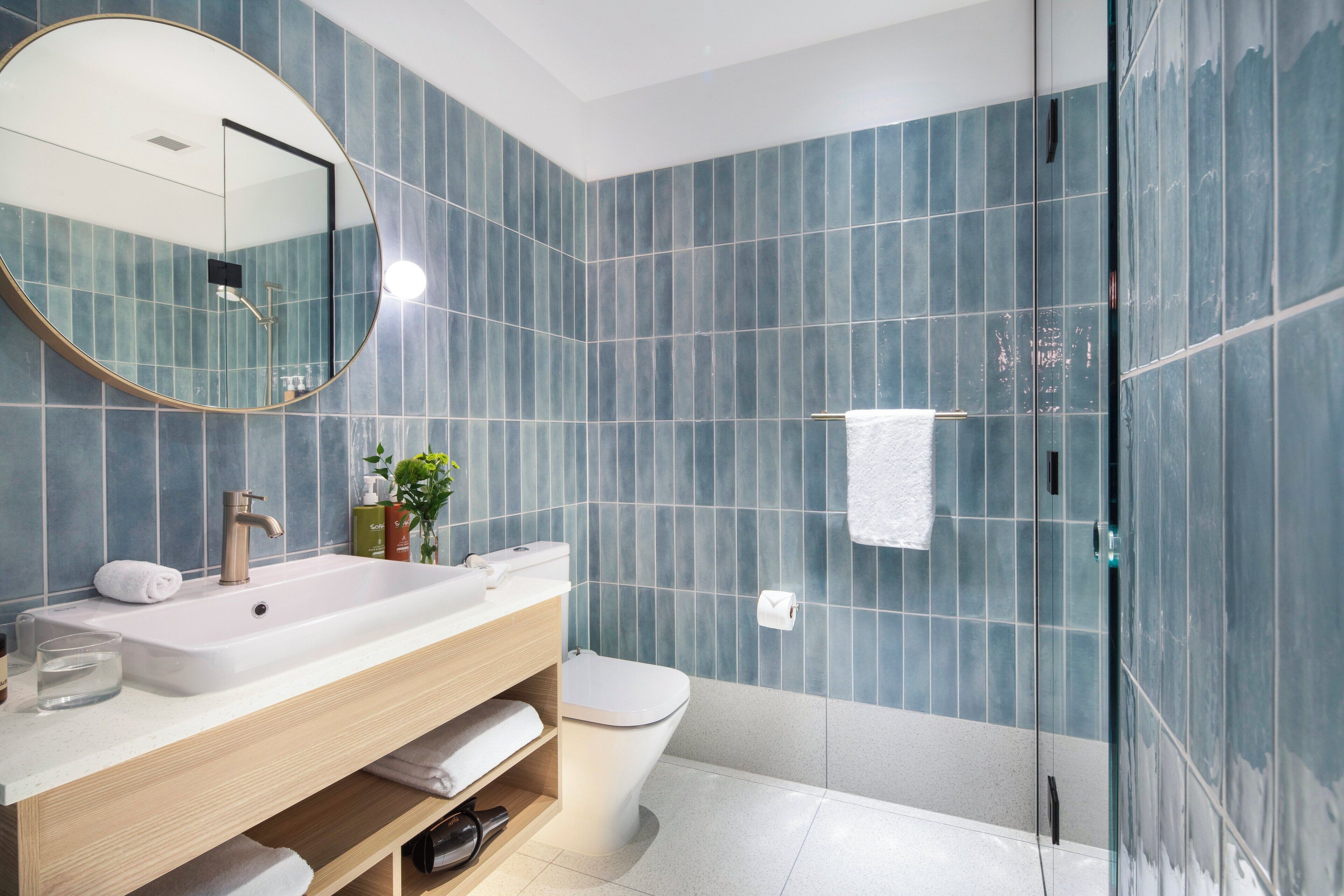 A modern bathroom with a large mirror, white sink, and a glass shower enclosure.