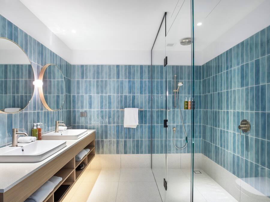 Un baño moderno con dos lavamanos, cabina de ducha de vidrio y un espejo grande.