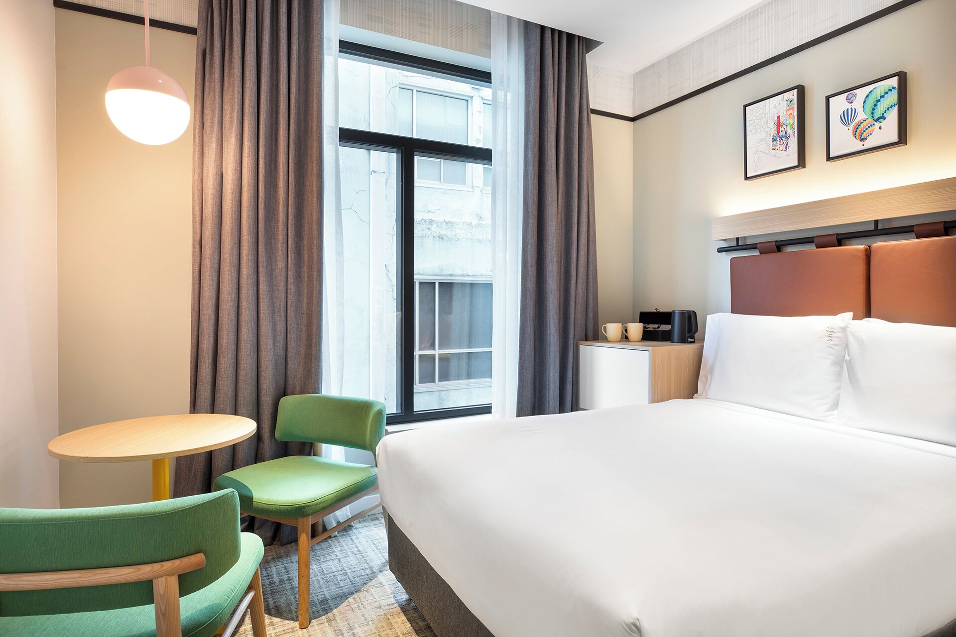 Quarto de hotel com uma cama grande, uma escrivaninha com cadeira, uma janela com cortinas e obras de arte na parede.