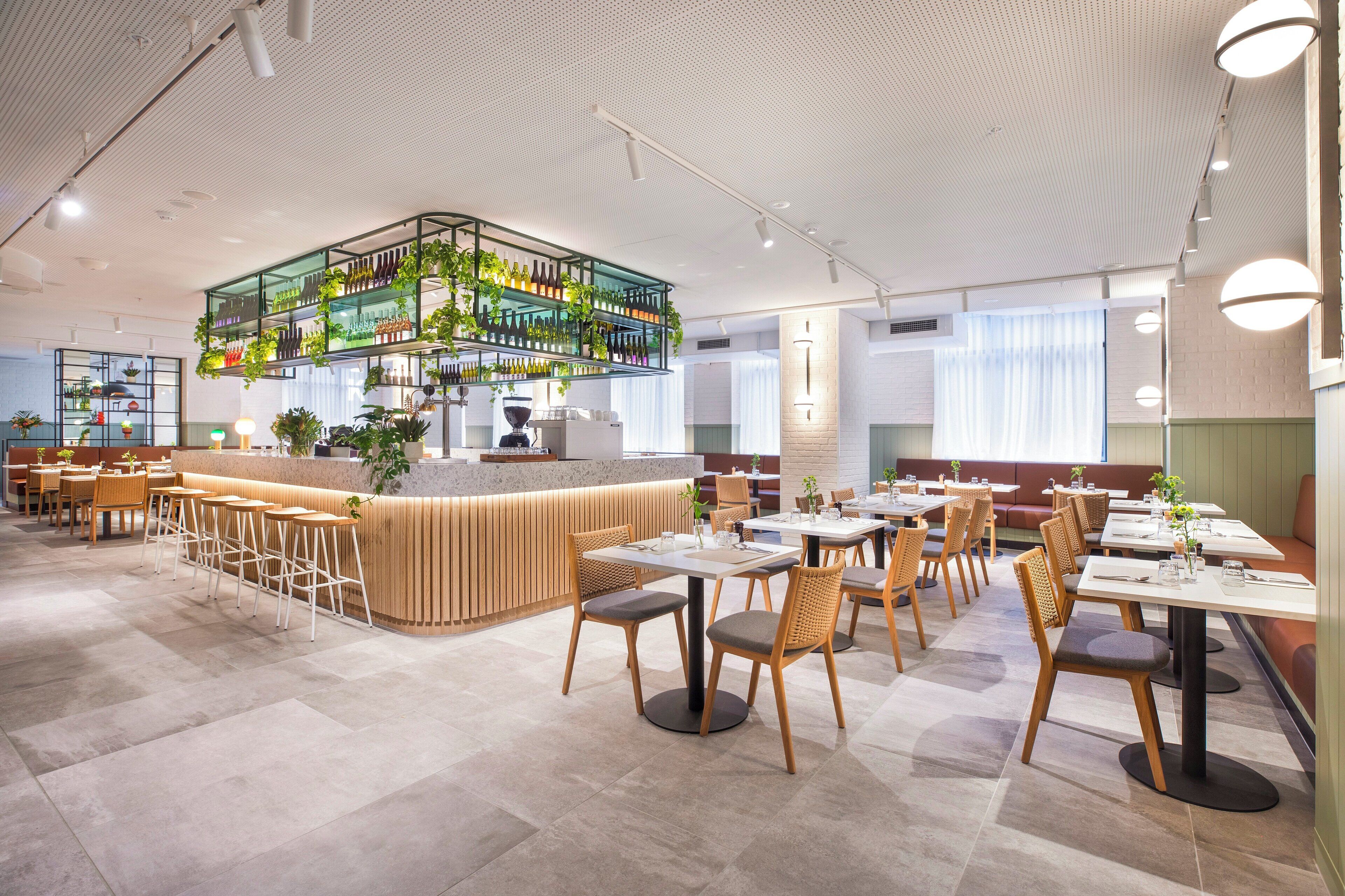 A modern restaurant interior with a central bar area, multiple seating options, and a ceiling with a unique pattern.